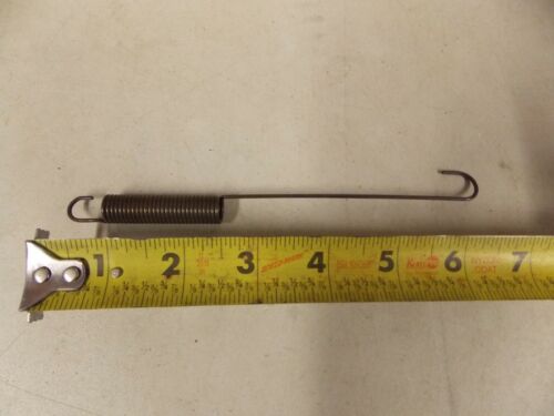A metal spring with hooks on both ends next to a measuring tape.