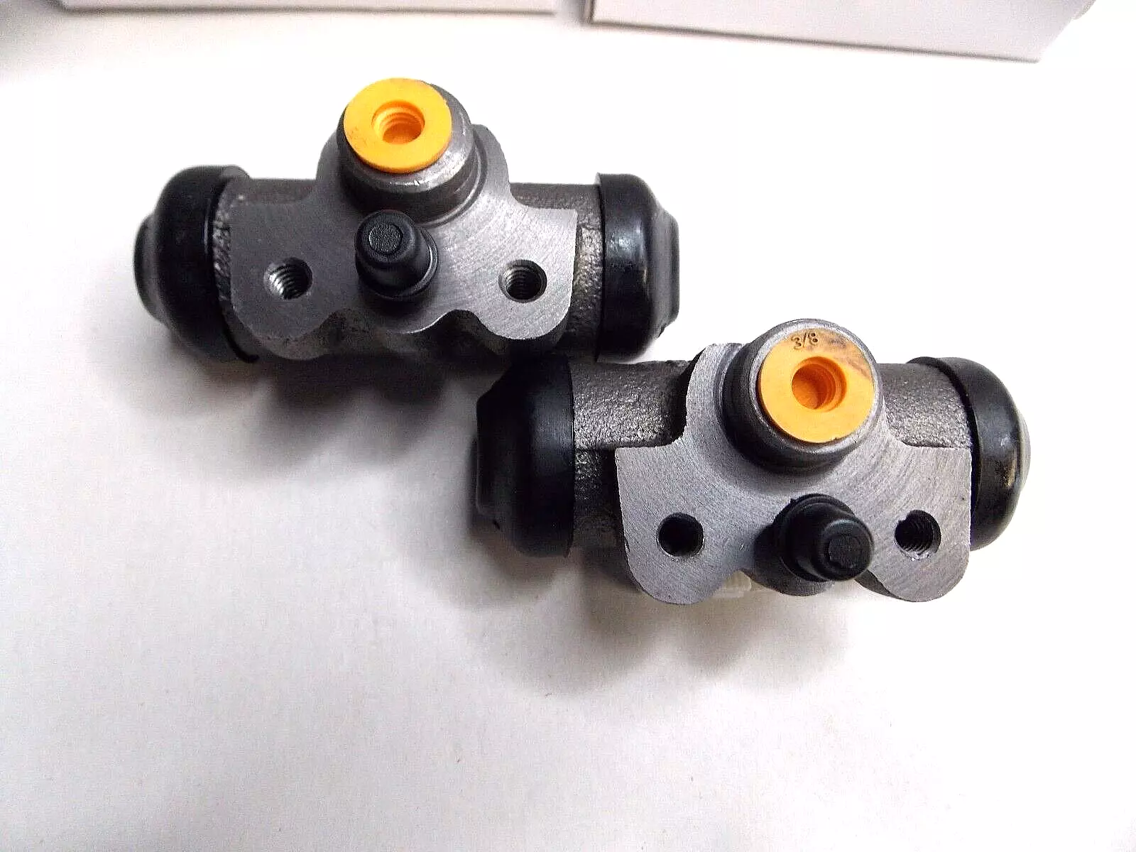 Two black and silver mechanical brake cylinders with orange caps.