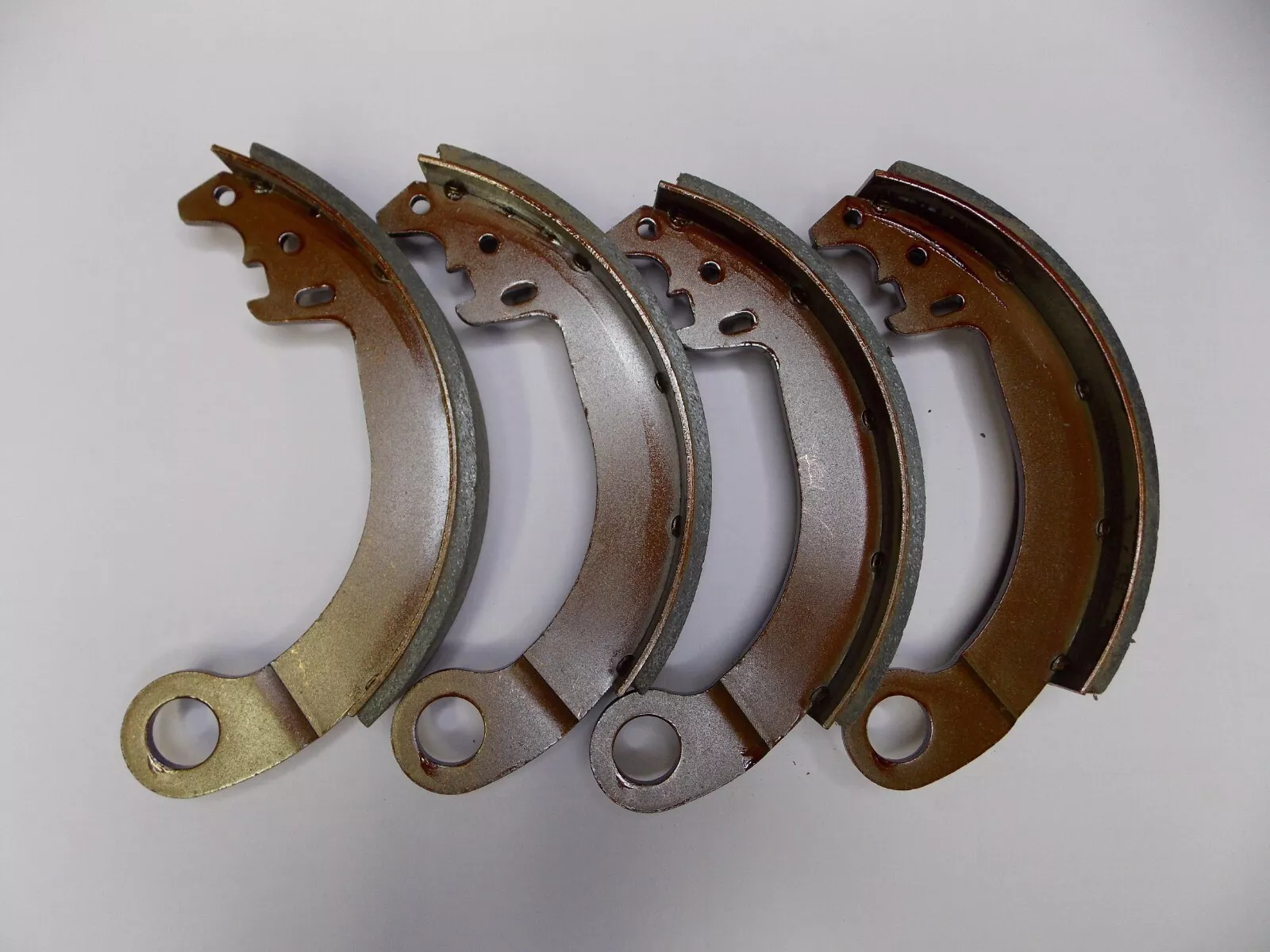 Four brake shoes lined up in a row on a white surface.